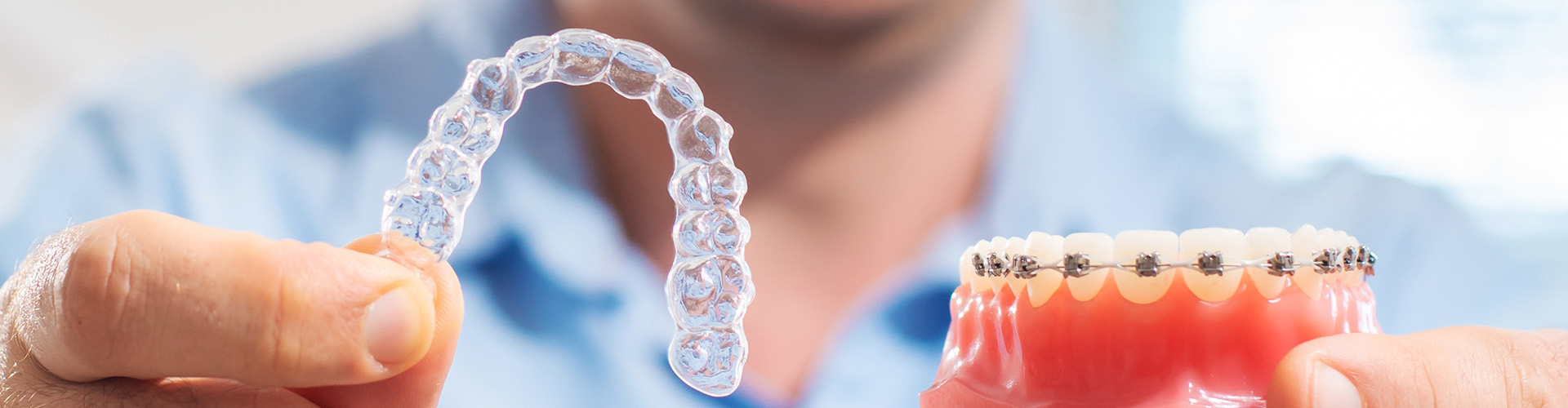 man holding clear aligner in one hand and braces on a mouth model in the other
