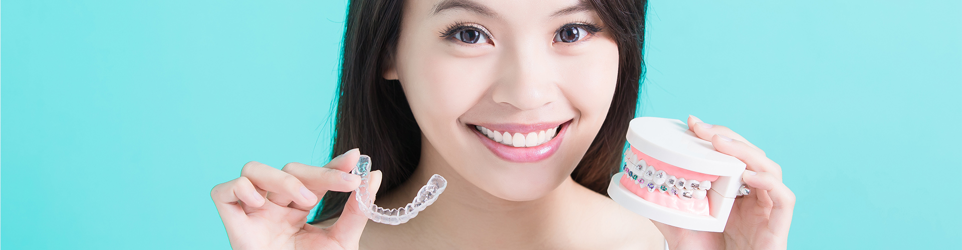 smiling woman holding clear aligner and braces model