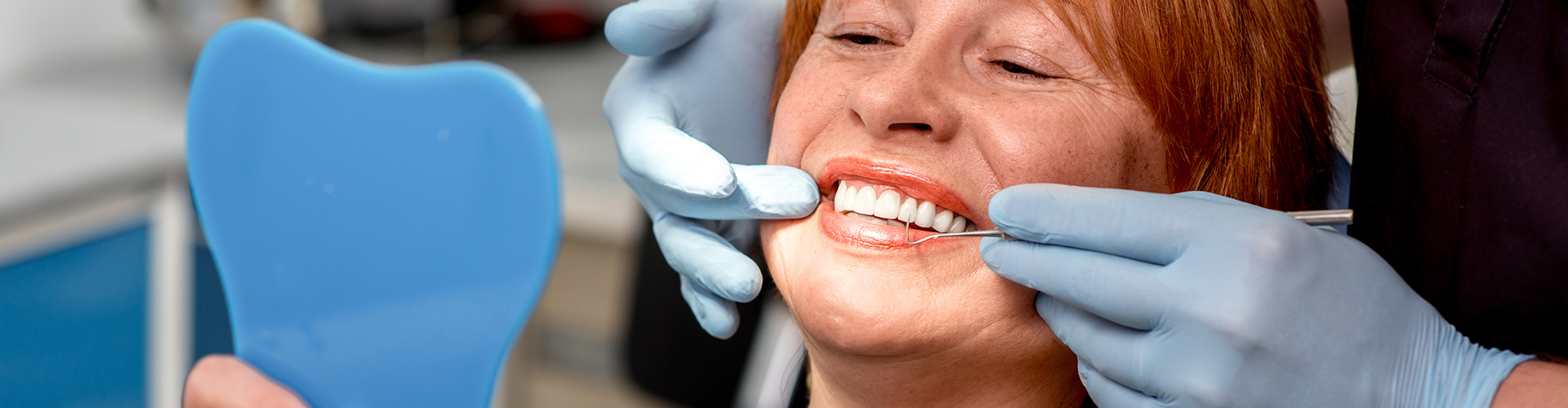 gloved hands on the side of smiling woman's mouth as she looks in mirror